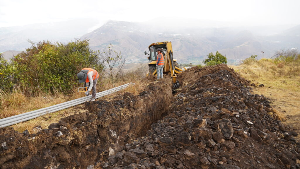 Trabajadores instalan tuberías del nuevo sistema de agua potable de Pimampiro junto a una excavadora.