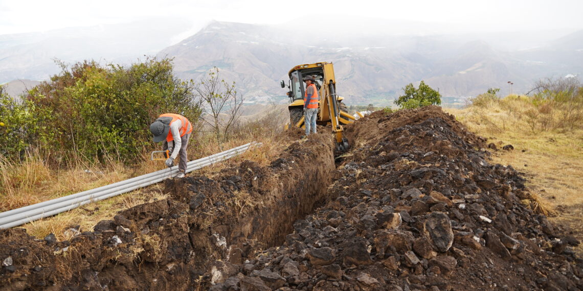 Trabajadores instalan tuberías del nuevo sistema de agua potable de Pimampiro junto a una excavadora.