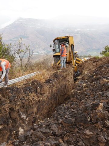 Trabajadores instalan tuberías del nuevo sistema de agua potable de Pimampiro junto a una excavadora.
