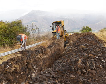 Trabajadores instalan tuberías del nuevo sistema de agua potable de Pimampiro junto a una excavadora.