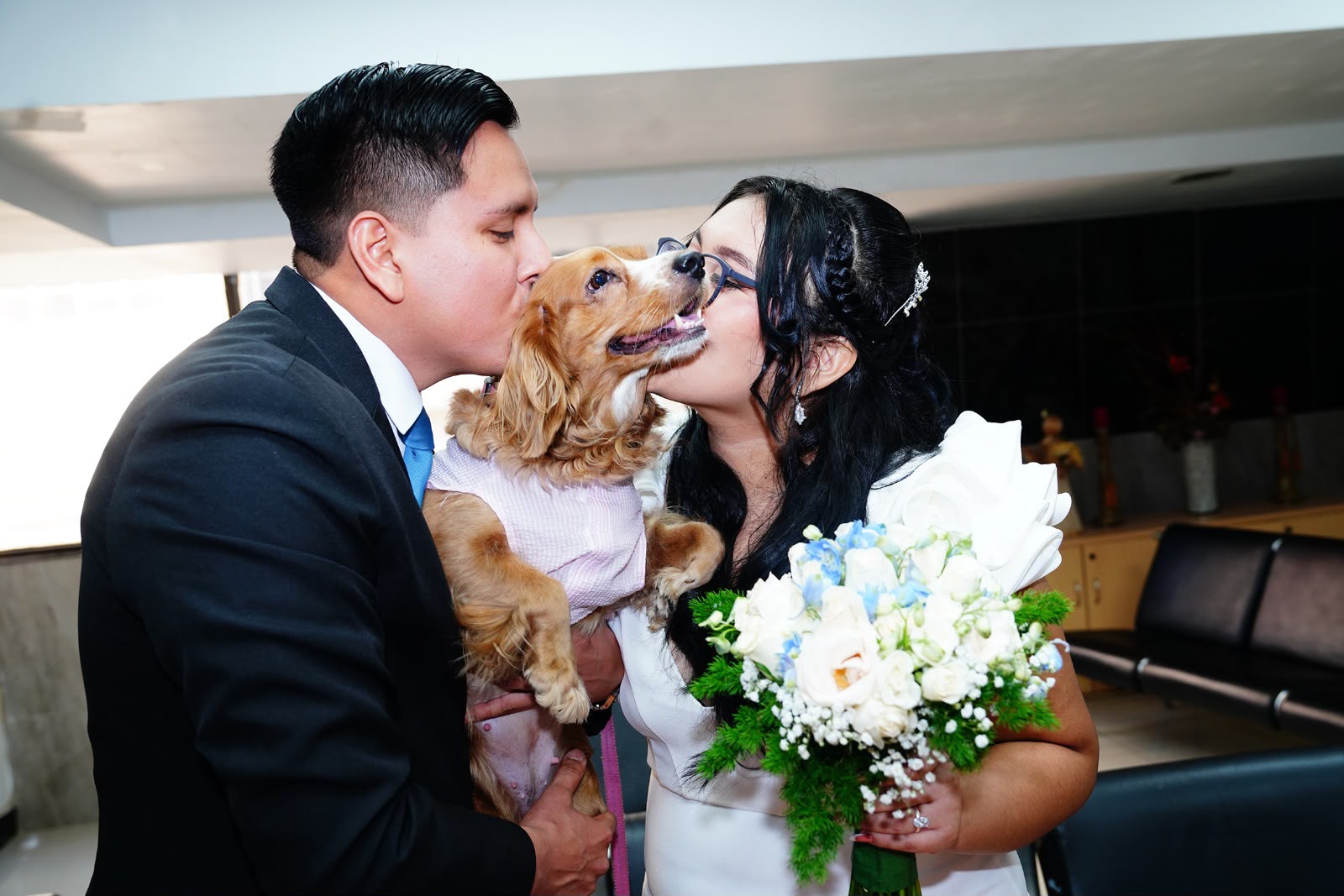 Una pareja de novios sostiene y besa a su perro en una fotografía de boda.