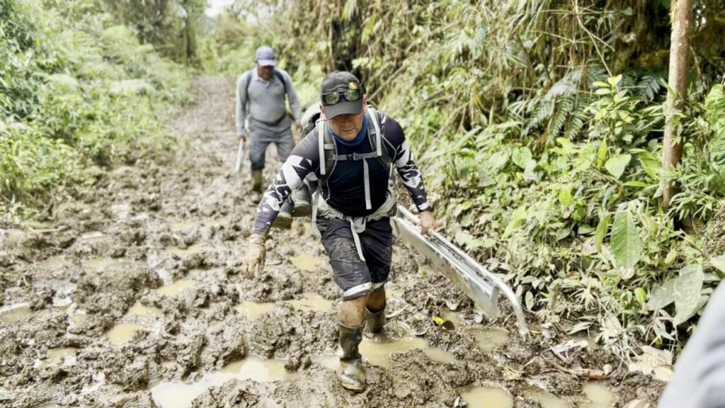 Integrantes de la brigada caminan por un sendero lodoso y transportan una camilla plegada desde San Francisco de Palmira hasta Ibarra.